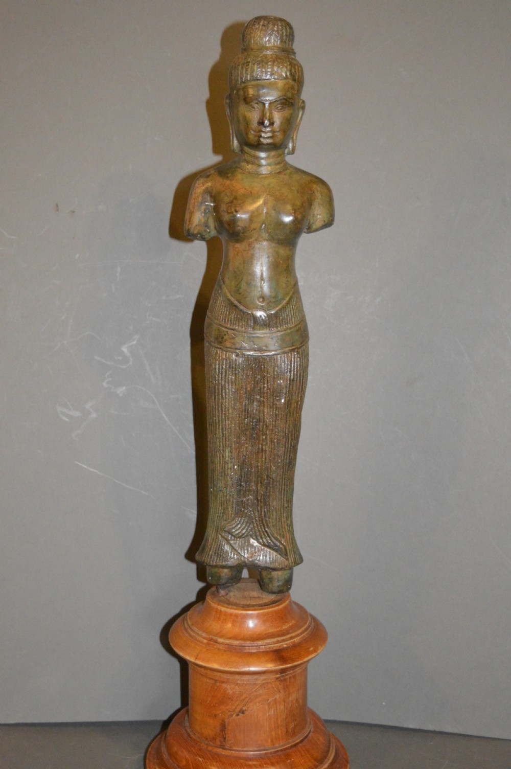 A standing patinated bronze figure of a Buddhist deity mounted on a turned wooden socle base.