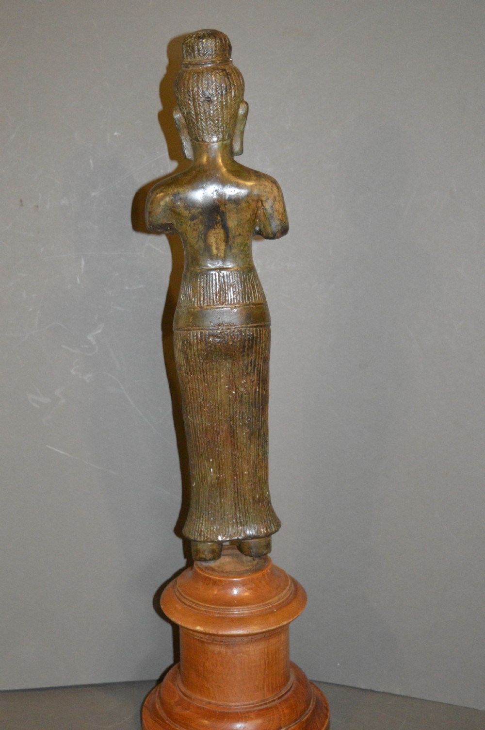 A standing patinated bronze figure of a Buddhist deity mounted on a turned wooden socle base. View X