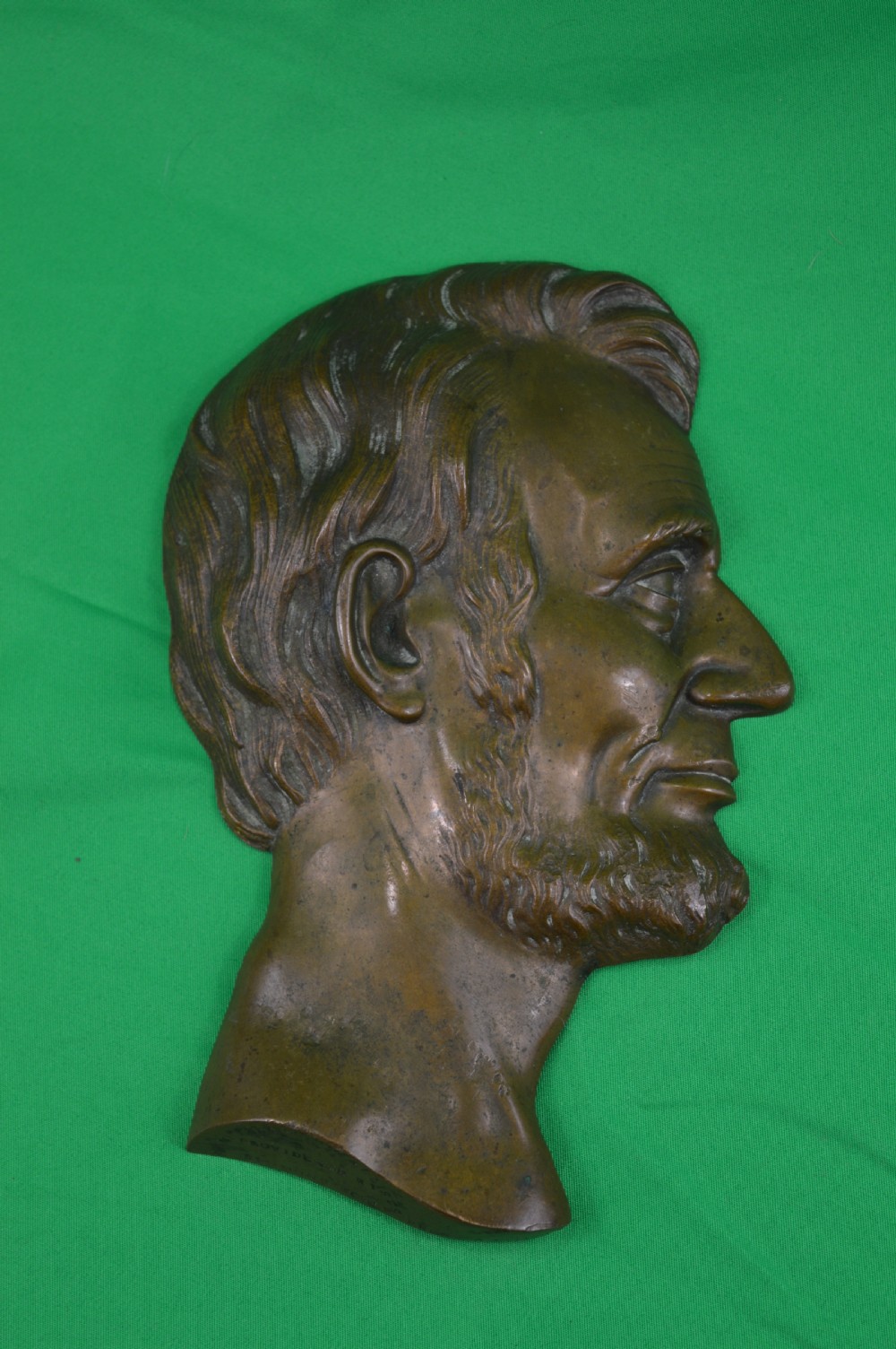 A cast bronze relief profile plaque depicting Abraham Lincoln in right-facing profile with a patinated dark brown surface.