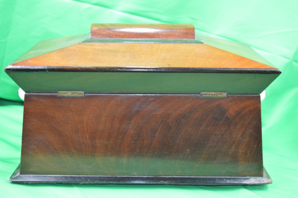 A Regency mahogany tea caddy featuring a tapered sarcophagus shape, stepped hinged lid, and central brass keyhole escutcheon. View IX