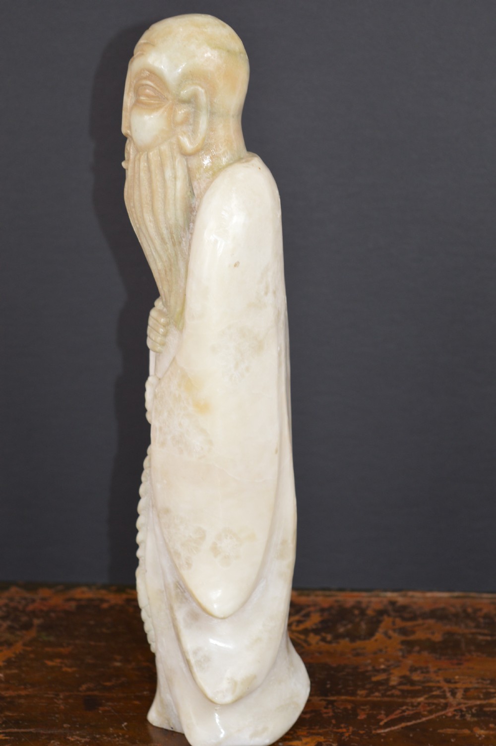 A cream-coloured carved hardstone sculpture depicting a standing bearded Chinese sage in long flowing robes holding a fish on a cord. View IV