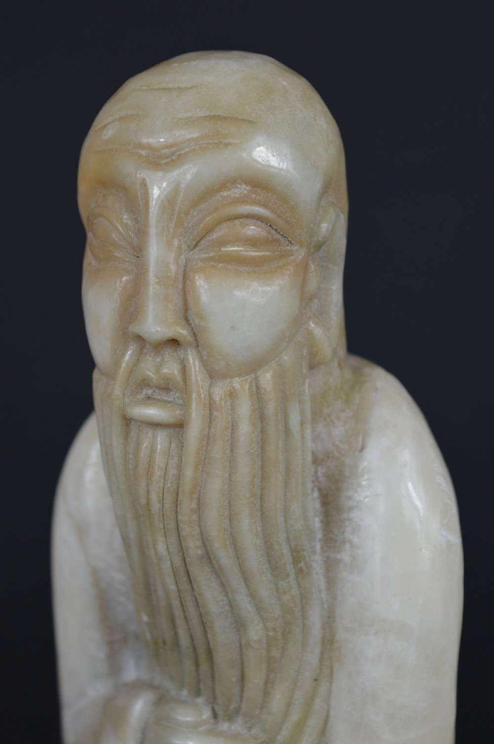 A cream-coloured carved hardstone sculpture depicting a standing bearded Chinese sage in long flowing robes holding a fish on a cord. View V