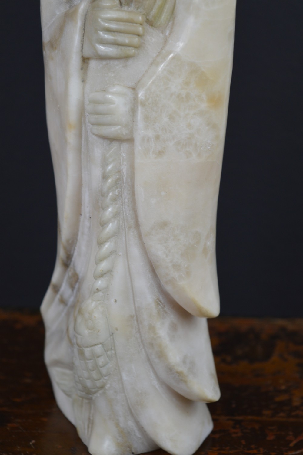 A cream-coloured carved hardstone sculpture depicting a standing bearded Chinese sage in long flowing robes holding a fish on a cord. View VII
