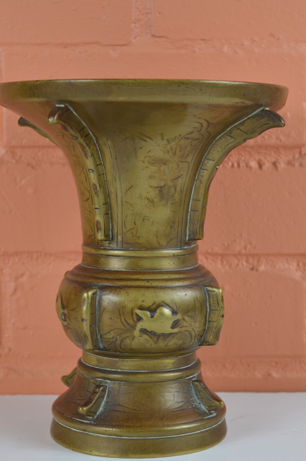 A cast bronze trumpet-shaped Chinese Gu vase with vertical flanges, a bulbous central section, and incised archaic pattern detailing.
