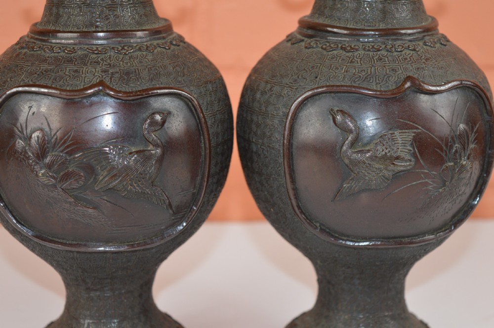 A pair of dark brown patinated Japanese bronze vases featuring dragon-form handles and relief panels depicting birds amongst aquatic foliage. View II