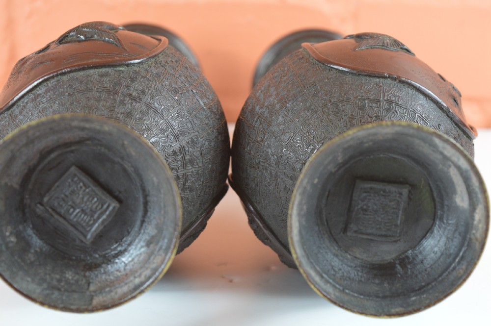 A pair of dark brown patinated Japanese bronze vases featuring dragon-form handles and relief panels depicting birds amongst aquatic foliage. View III