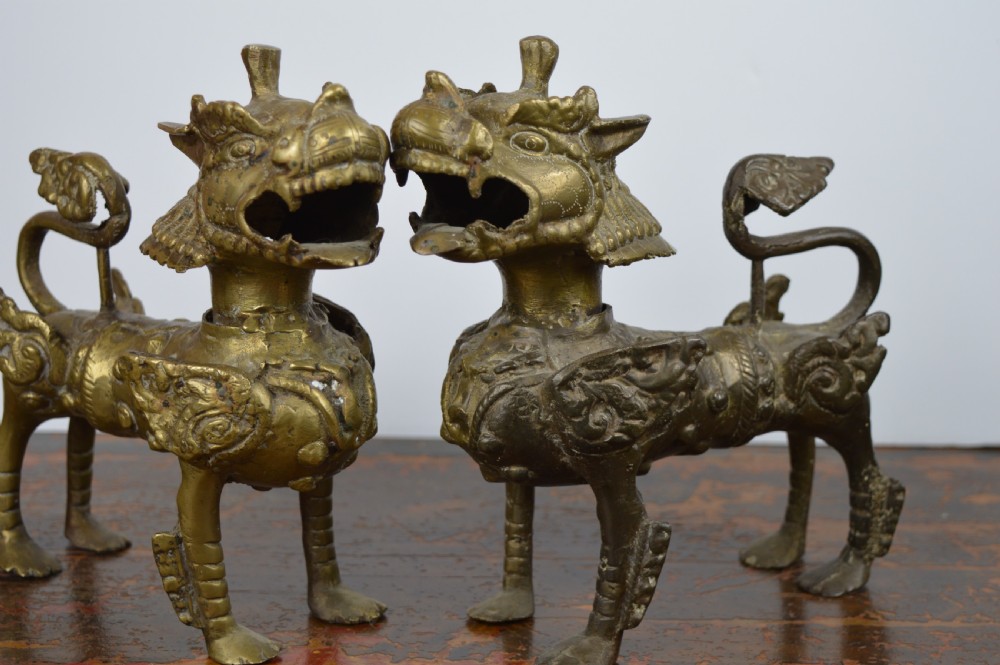 A pair of antique cast gilt bronze Tibetan temple lions featuring open mouths, chased body detail, and raised tails.