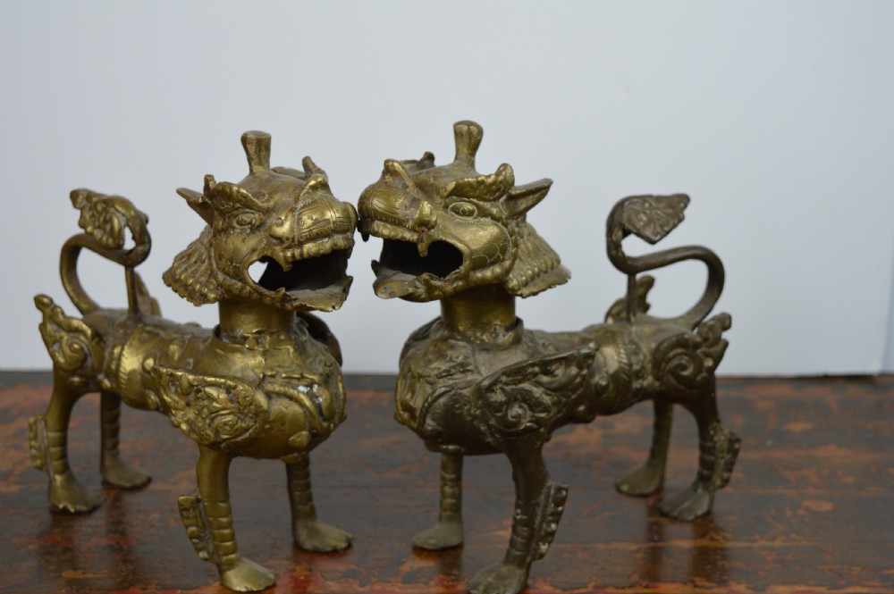 A pair of antique cast gilt bronze Tibetan temple lions featuring open mouths, chased body detail, and raised tails. View II