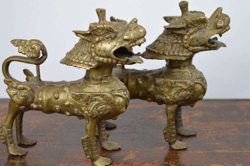 A pair of antique cast gilt bronze Tibetan temple lions featuring open mouths, chased body detail, and raised tails. View IV
