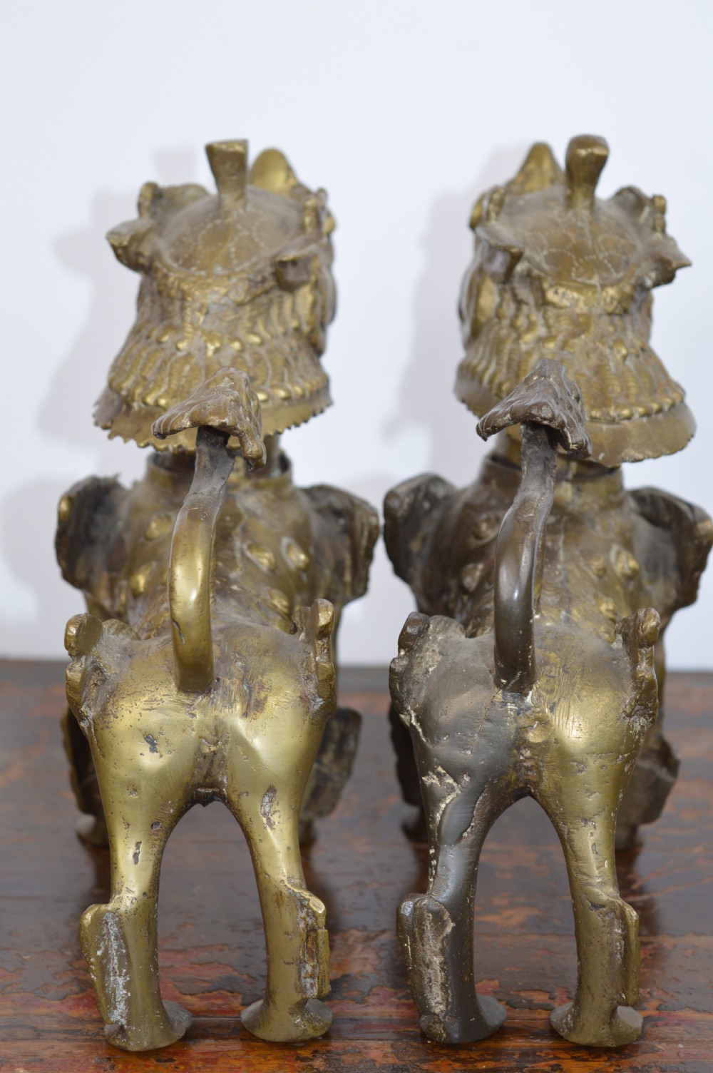 A pair of antique cast gilt bronze Tibetan temple lions featuring open mouths, chased body detail, and raised tails. View VI