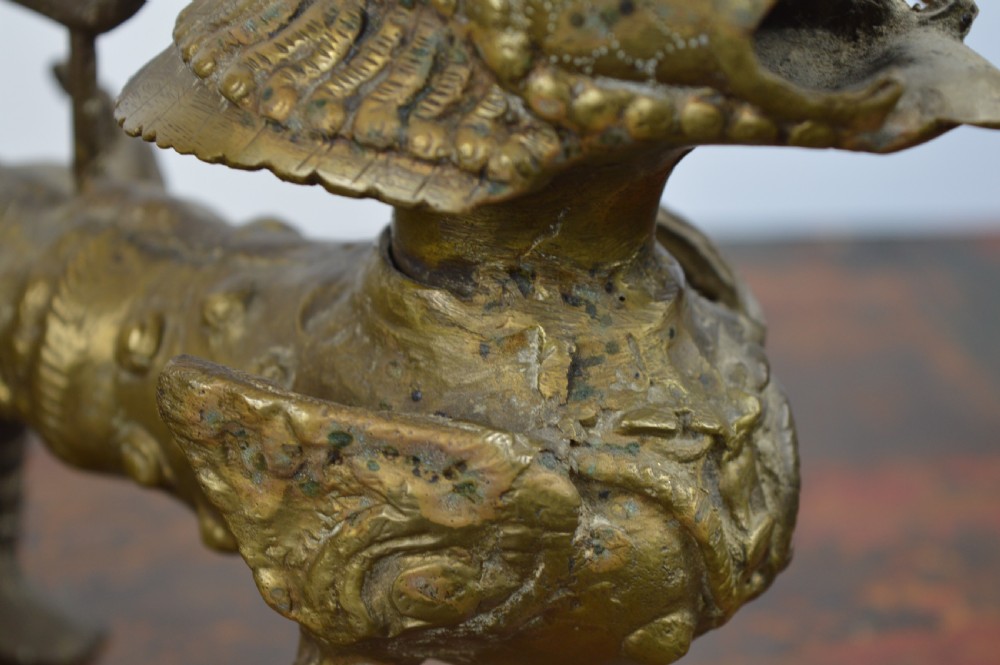 A pair of antique cast gilt bronze Tibetan temple lions featuring open mouths, chased body detail, and raised tails. View X