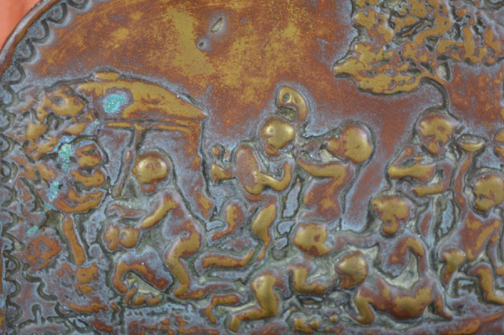 An antique embossed brass hanging spill box featuring detailed cherub motifs in repousse relief and an arched mounting backplate. View II