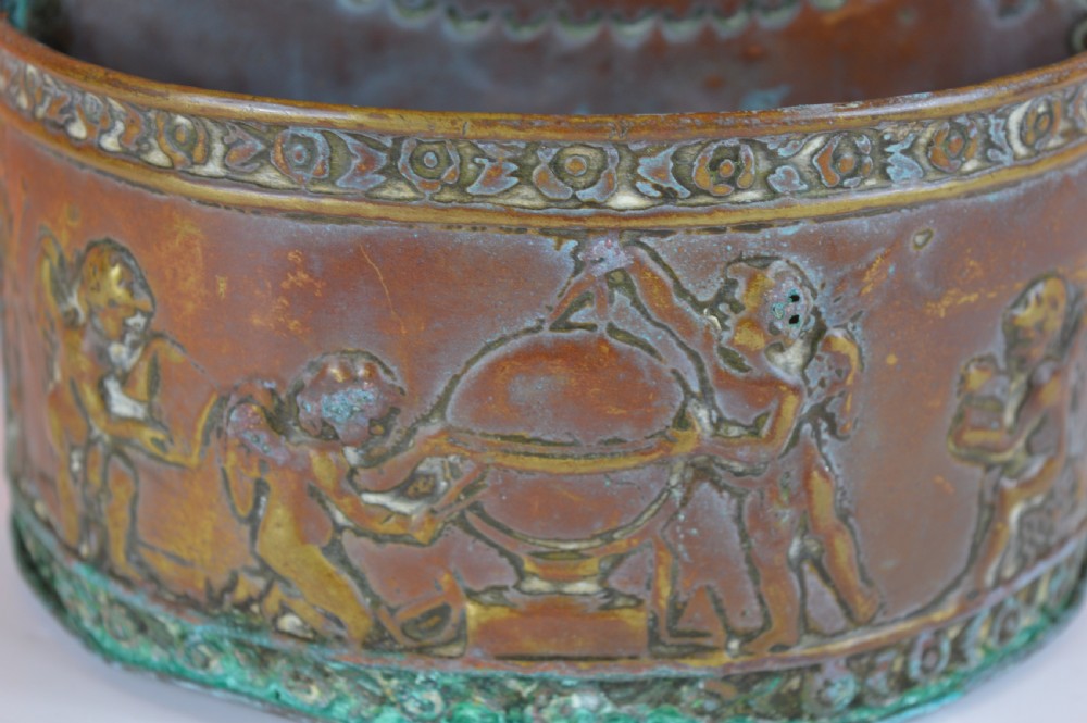 An antique embossed brass hanging spill box featuring detailed cherub motifs in repousse relief and an arched mounting backplate. View III