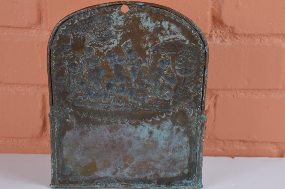 An antique embossed brass hanging spill box featuring detailed cherub motifs in repousse relief and an arched mounting backplate. View IV