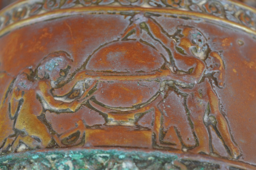 An antique embossed brass hanging spill box featuring detailed cherub motifs in repousse relief and an arched mounting backplate. View VI