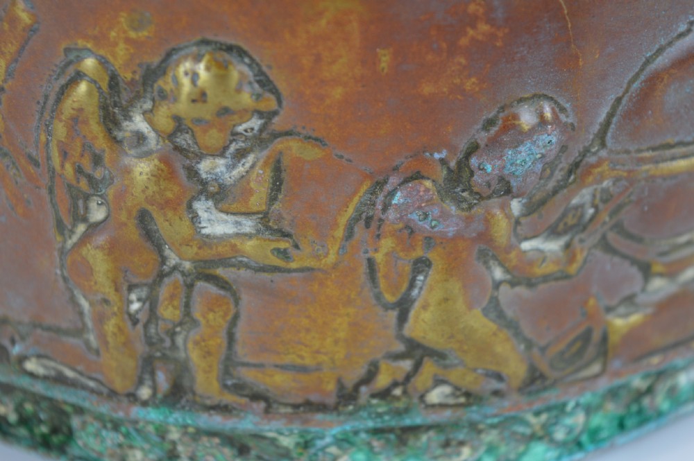 An antique embossed brass hanging spill box featuring detailed cherub motifs in repousse relief and an arched mounting backplate. View VIII