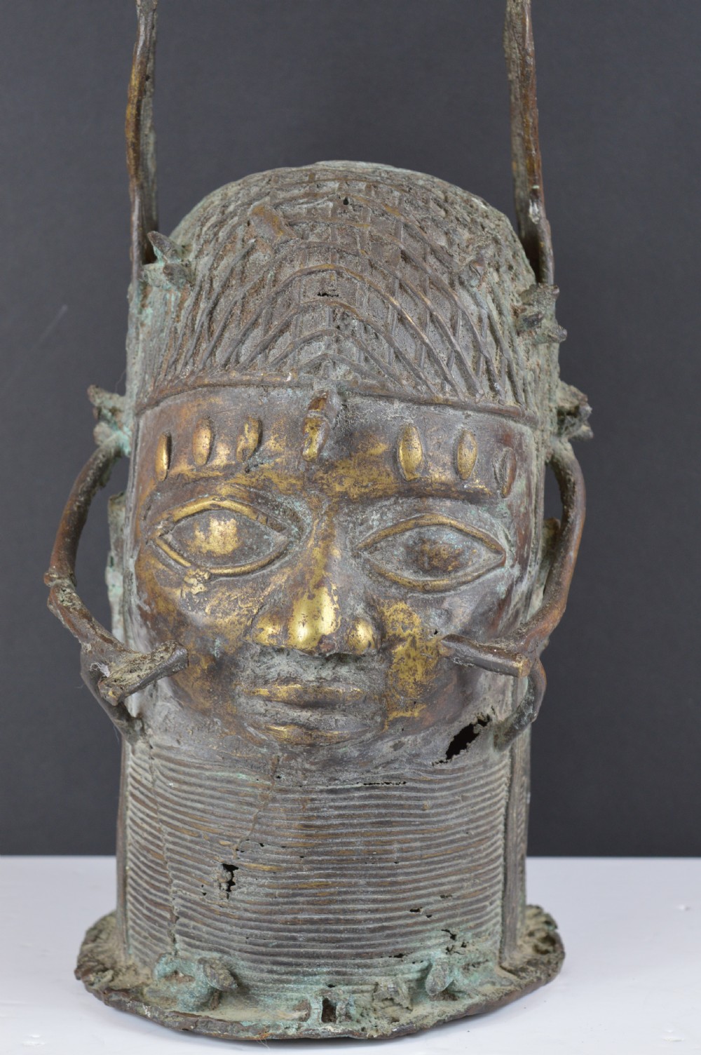 A cast bronze African bust featuring stylized facial features, a high ringed neck collar, and raised decorative elements on the headdress.