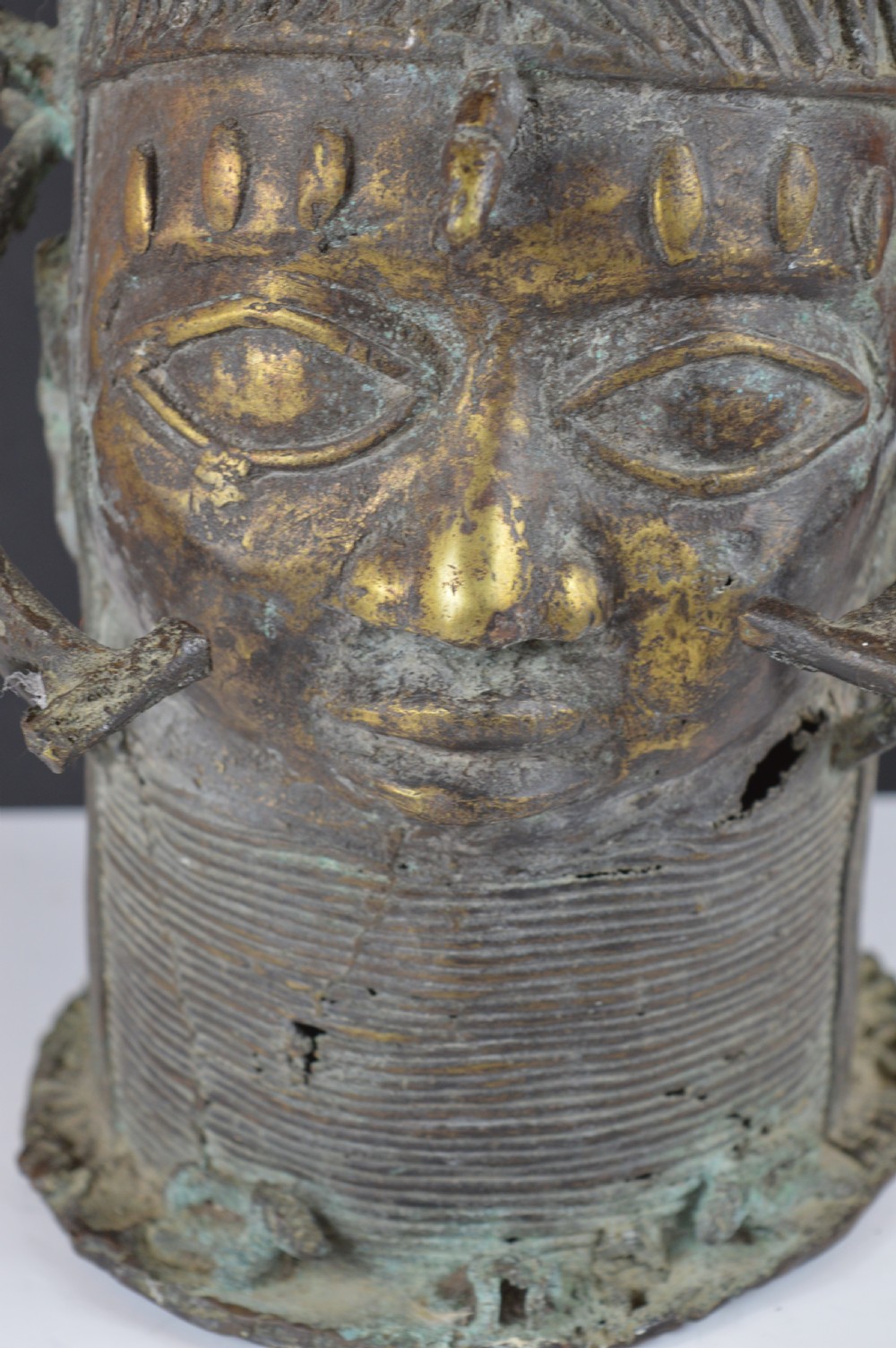 A cast bronze African bust featuring stylized facial features, a high ringed neck collar, and raised decorative elements on the headdress. View III