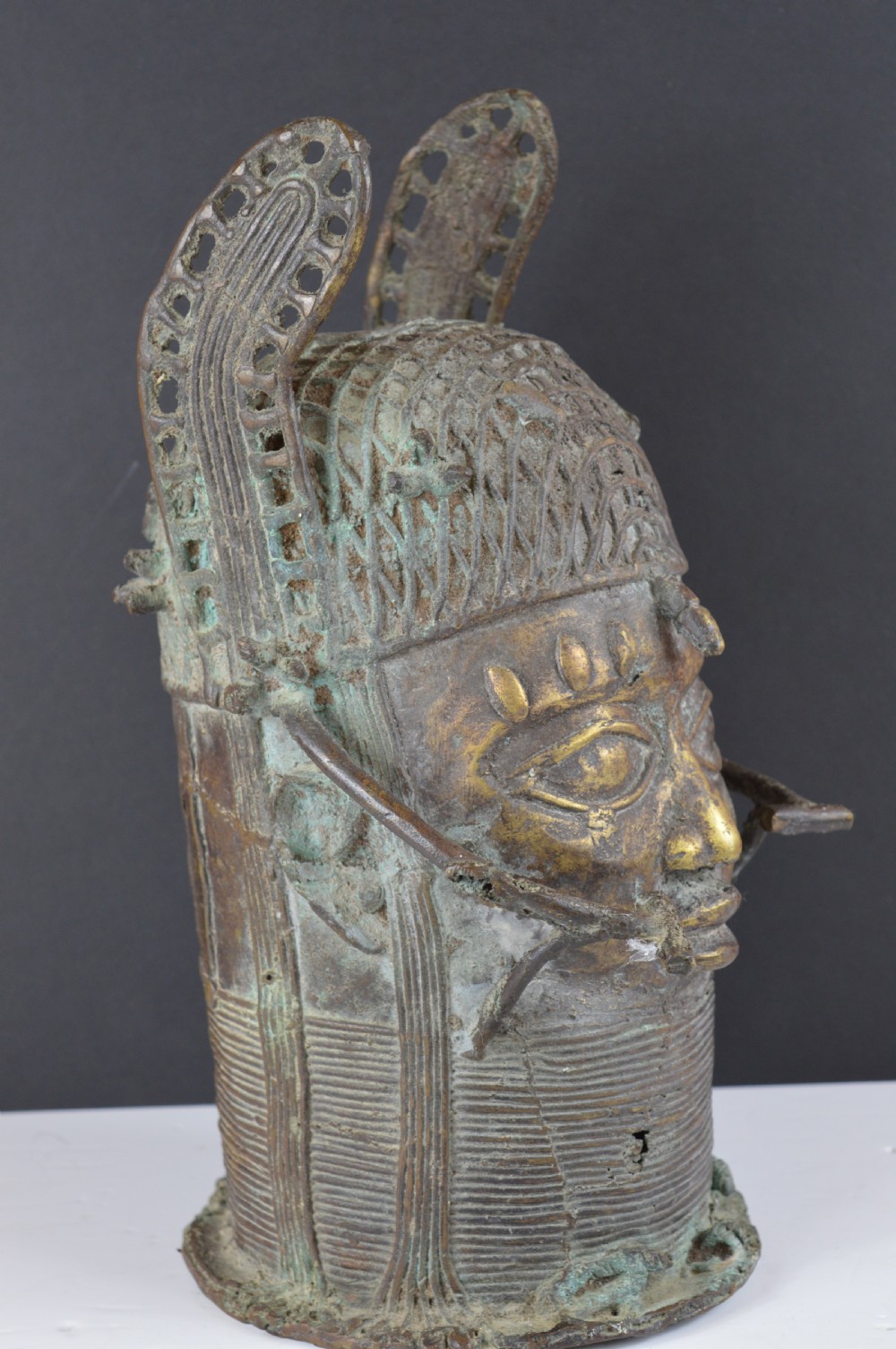 A cast bronze African bust featuring stylized facial features, a high ringed neck collar, and raised decorative elements on the headdress. View IV