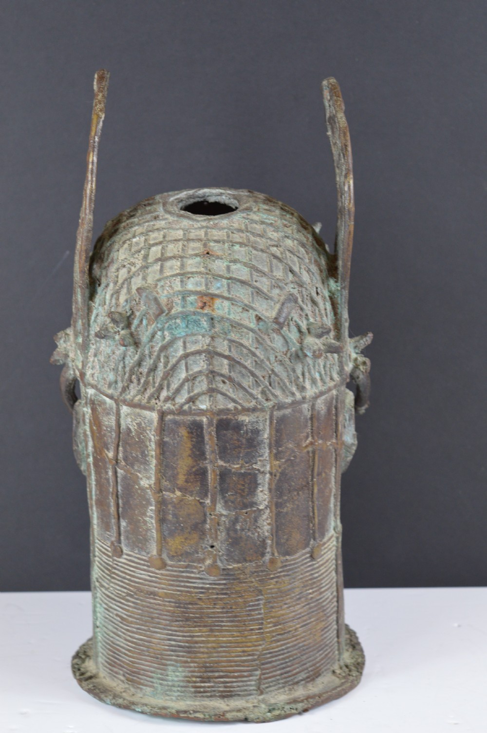 A cast bronze African bust featuring stylized facial features, a high ringed neck collar, and raised decorative elements on the headdress. View V