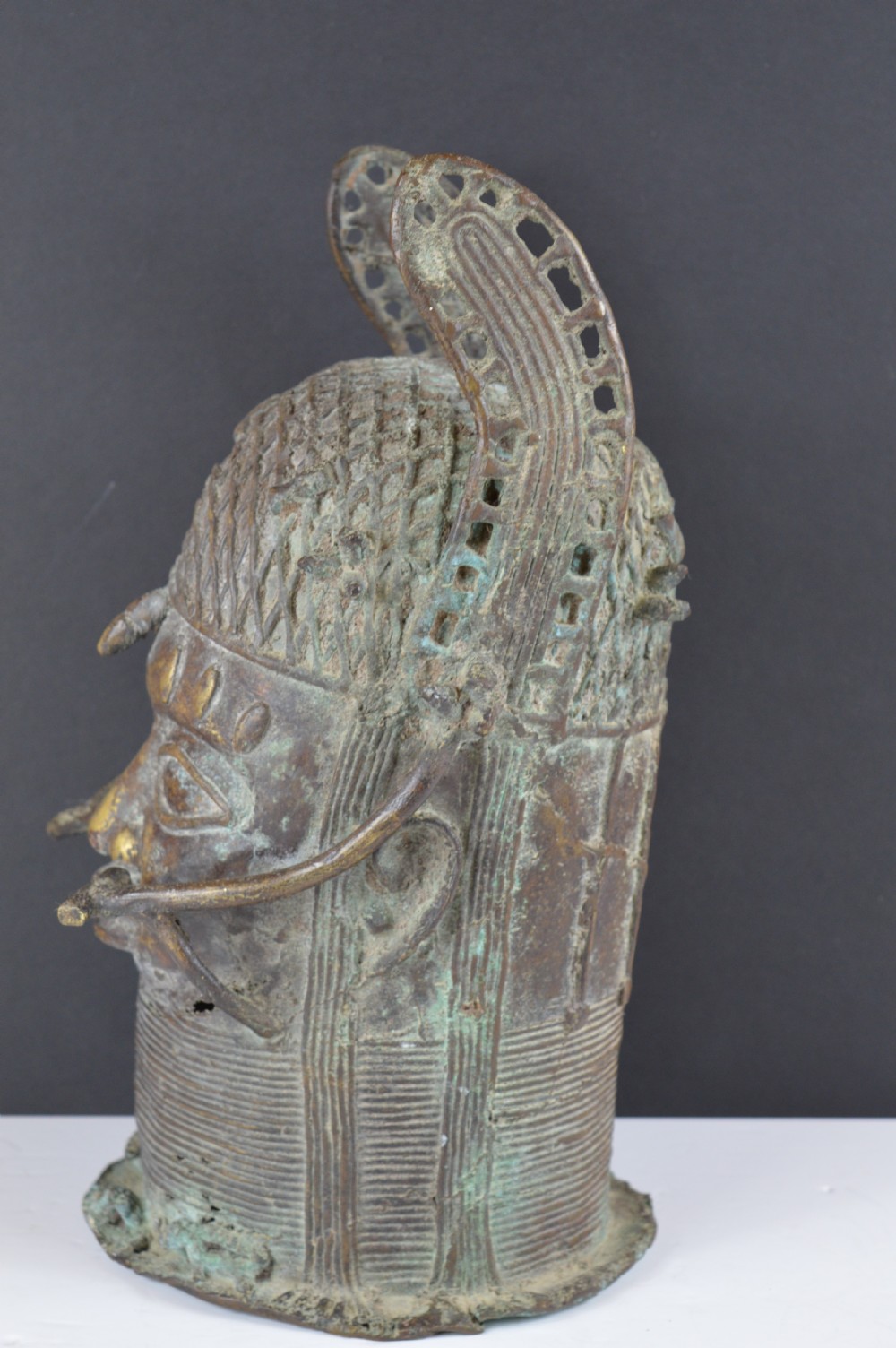 A cast bronze African bust featuring stylized facial features, a high ringed neck collar, and raised decorative elements on the headdress. View VI