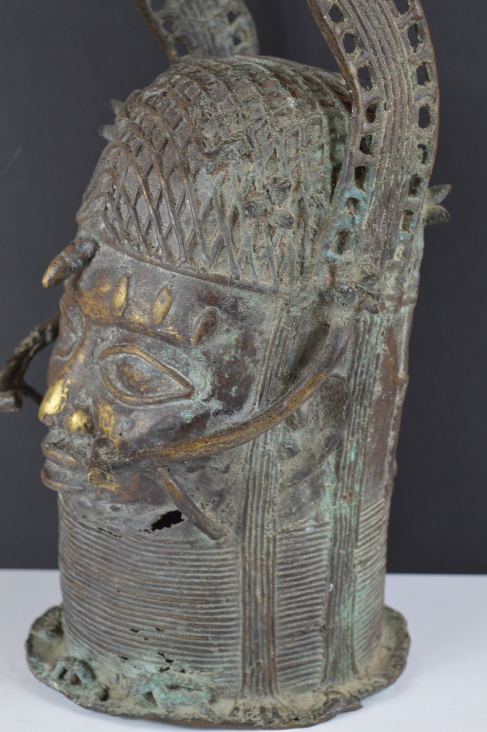 A cast bronze African bust featuring stylized facial features, a high ringed neck collar, and raised decorative elements on the headdress. View VII