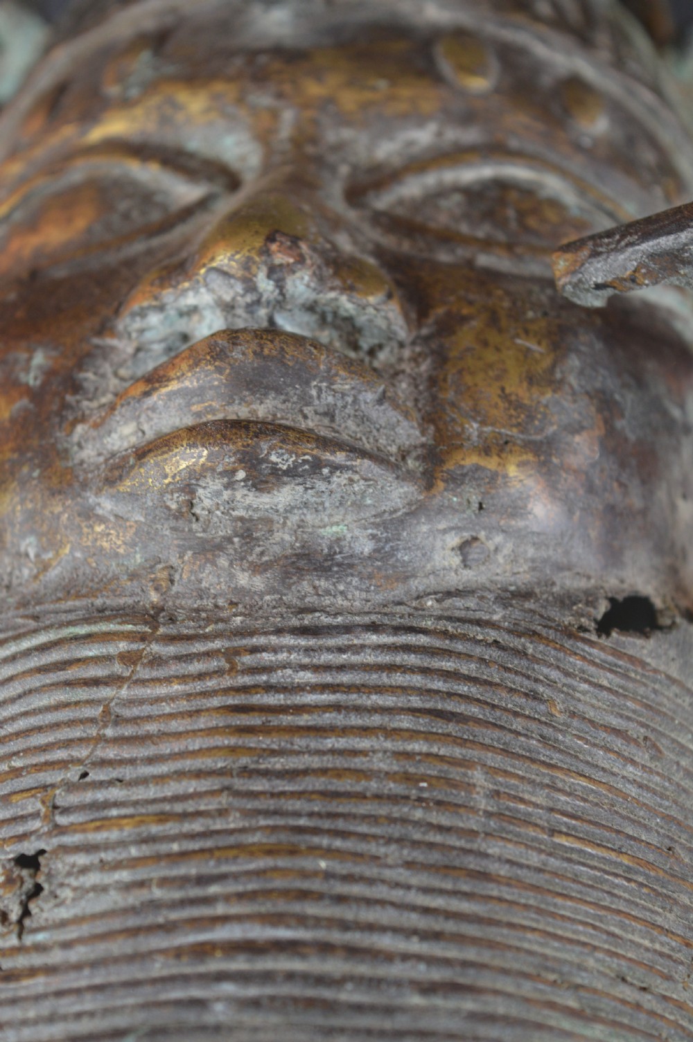 A cast bronze African bust featuring stylized facial features, a high ringed neck collar, and raised decorative elements on the headdress. View IX