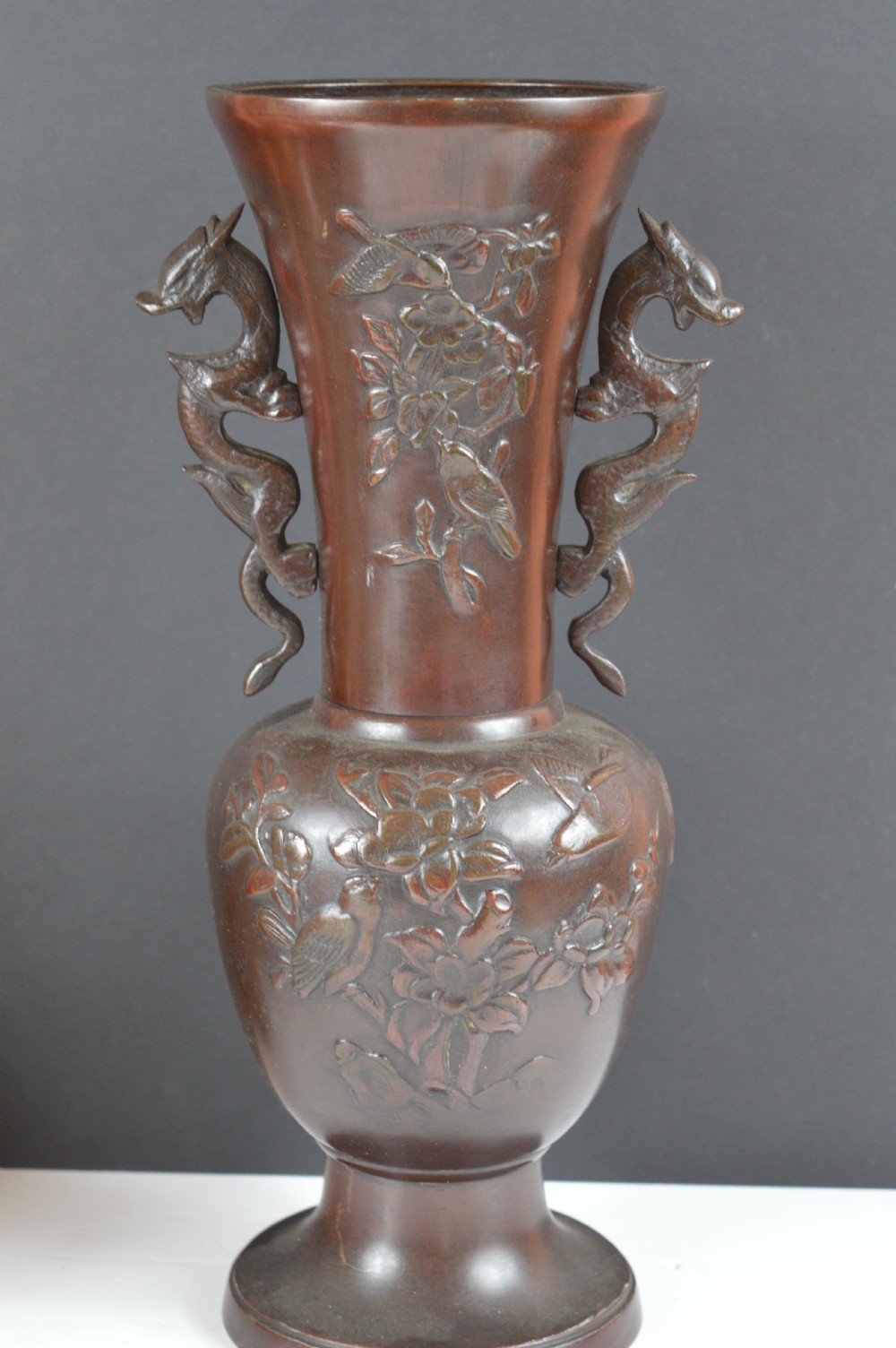 A cast dark bronze baluster vase featuring dragon-form side handles, a flared rim, and relief carvings of birds perched on flowering branches.