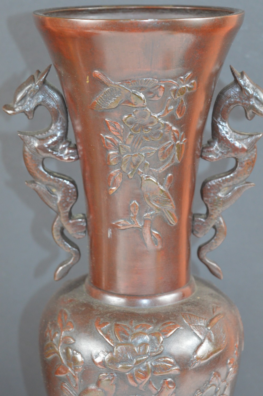 A cast dark bronze baluster vase featuring dragon-form side handles, a flared rim, and relief carvings of birds perched on flowering branches. View II