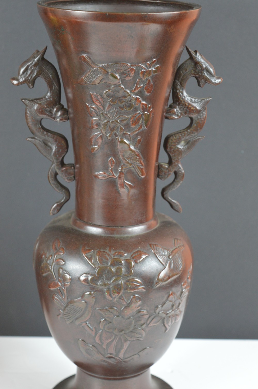 A cast dark bronze baluster vase featuring dragon-form side handles, a flared rim, and relief carvings of birds perched on flowering branches. View V
