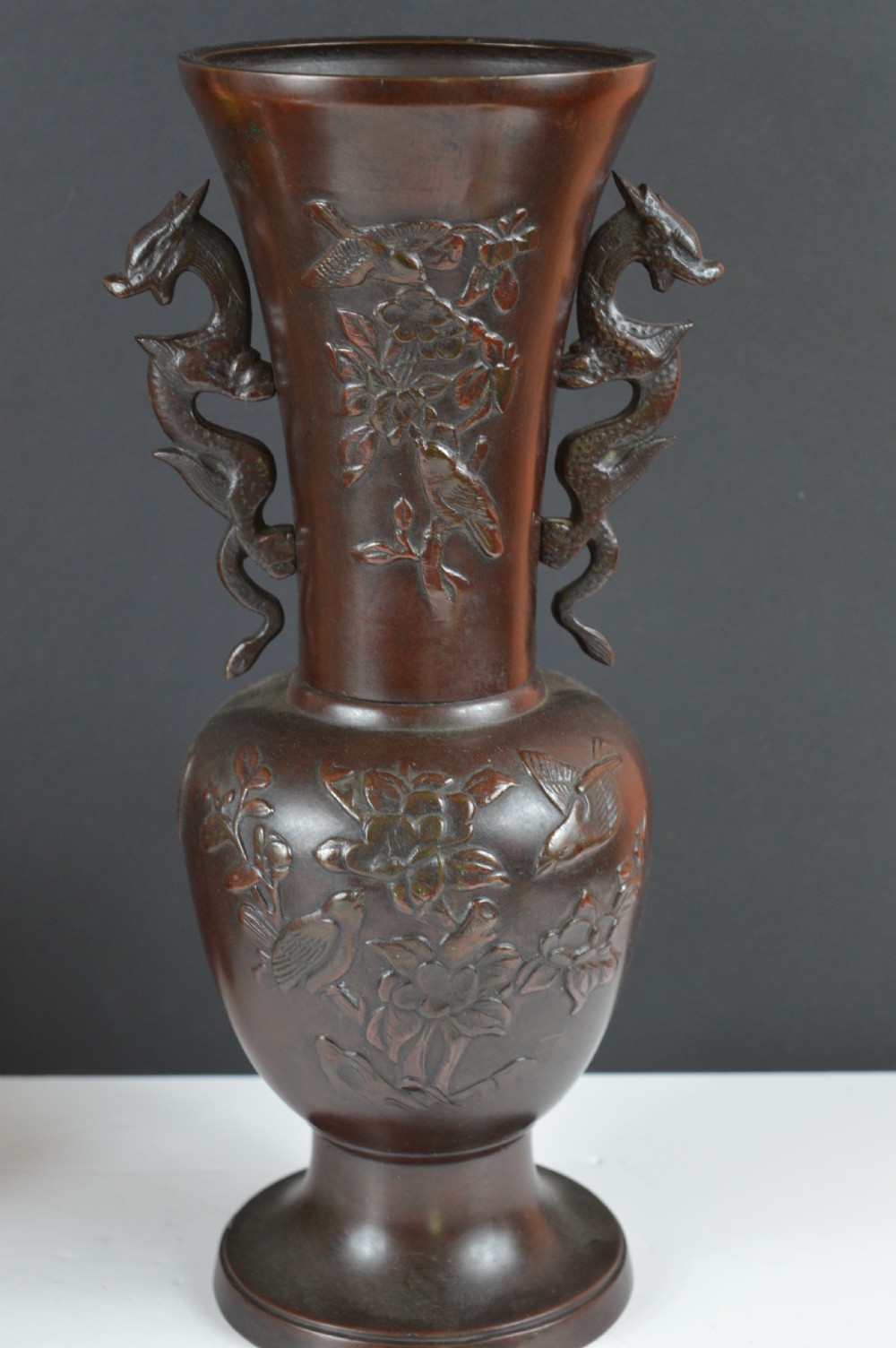 A cast dark bronze baluster vase featuring dragon-form side handles, a flared rim, and relief carvings of birds perched on flowering branches. View VI