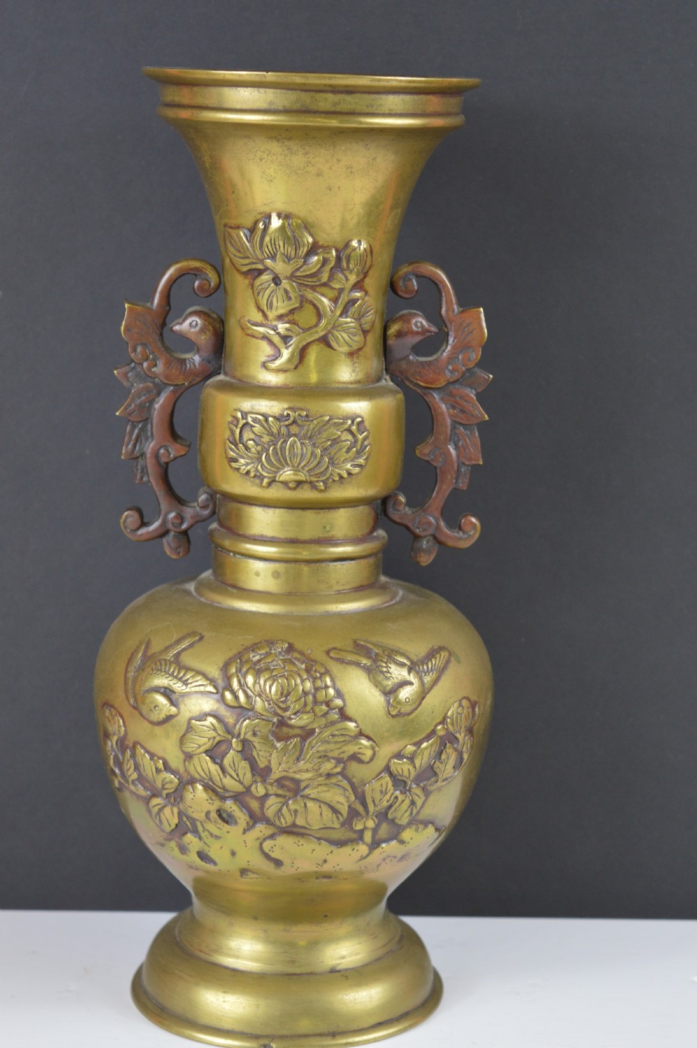 A cast bronze baluster vase featuring relief depictions of birds and flowers with bird-shaped side handles.