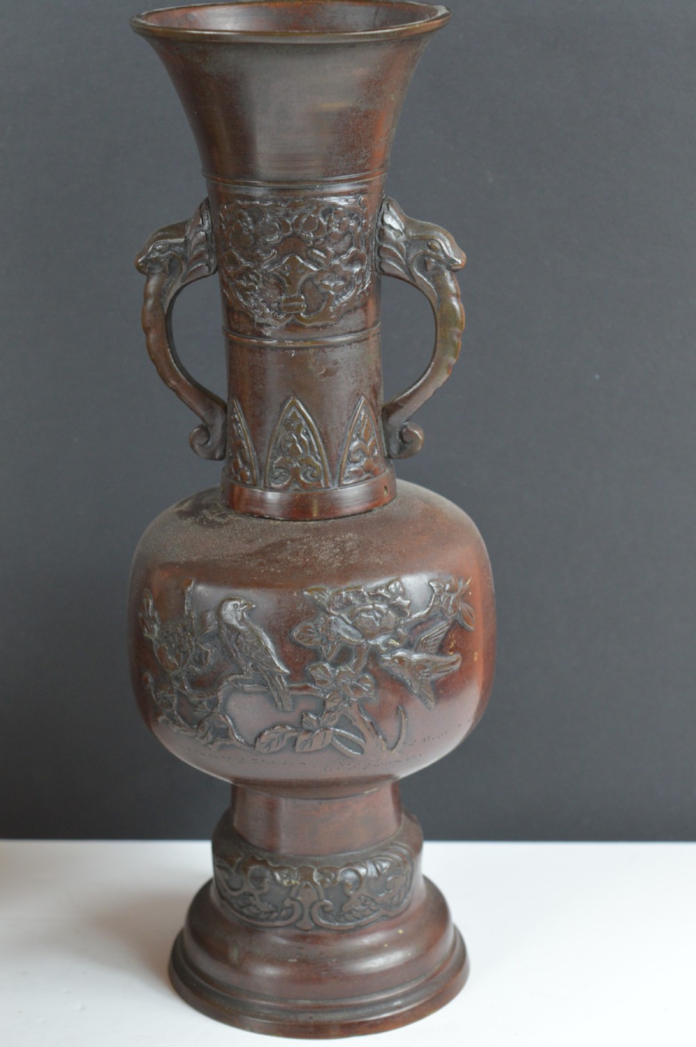 A dark brown patinated bronze vase with relief carvings of birds and flora, featuring flared rims and two stylized handles.