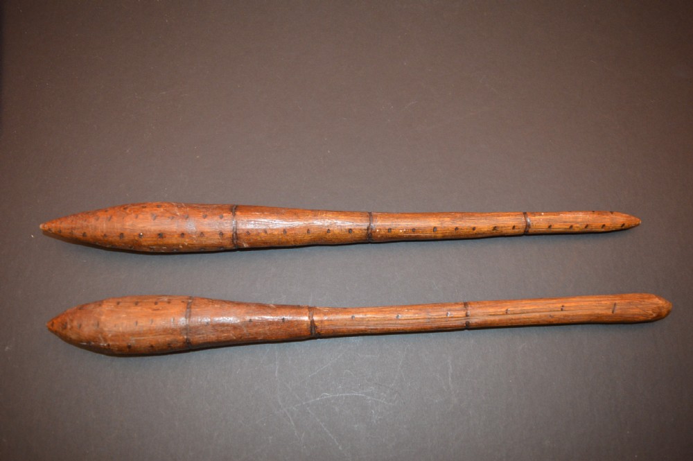 A pair of 19th-century carved Australian Aboriginal hardwood throwing clubs with pointed ends and incised dot decoration laid on a dark surface.