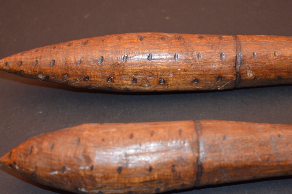 A pair of 19th-century carved Australian Aboriginal hardwood throwing clubs with pointed ends and incised dot decoration laid on a dark surface. View II