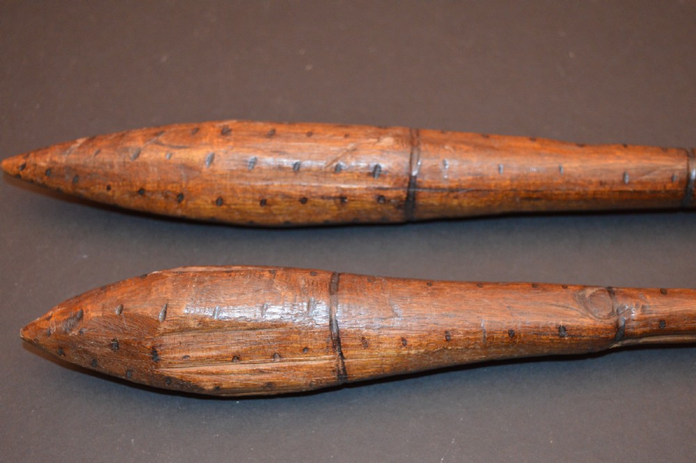 A pair of 19th-century carved Australian Aboriginal hardwood throwing clubs with pointed ends and incised dot decoration laid on a dark surface. View V