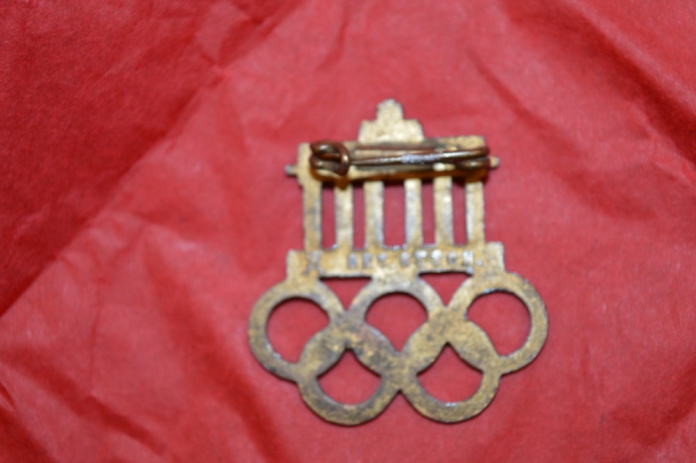 A 1936 Berlin Olympic Games enamel visitor badge featuring the Brandenburg Gate above five interconnected Olympic rings. View VII