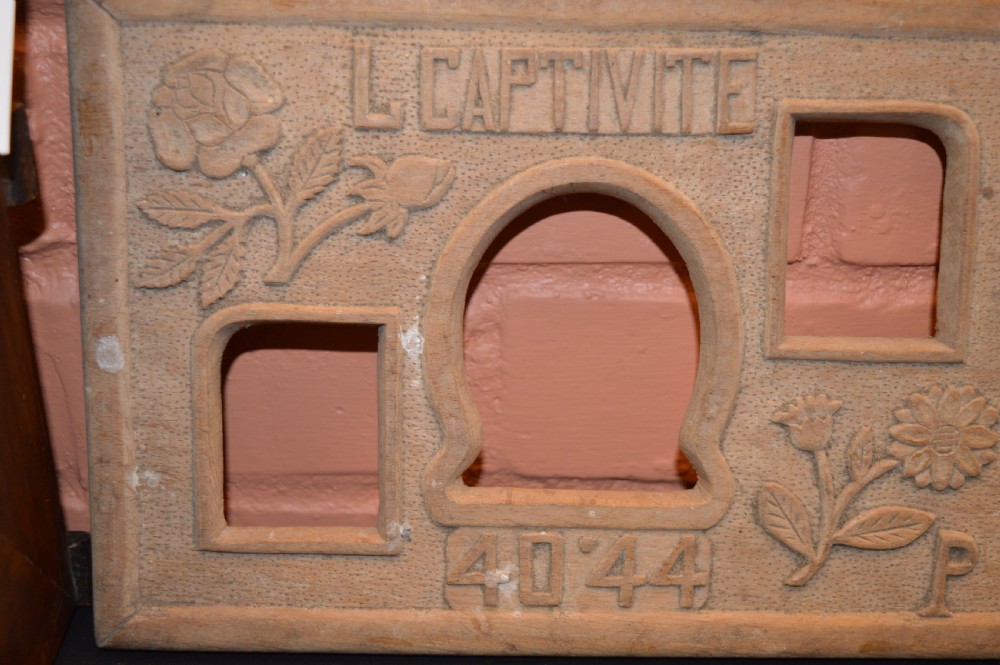 A four-piece collection of prisoner of war memorabilia including a carved wooden box, a wooden frame, a metal bell, and framed wartime documents. View V