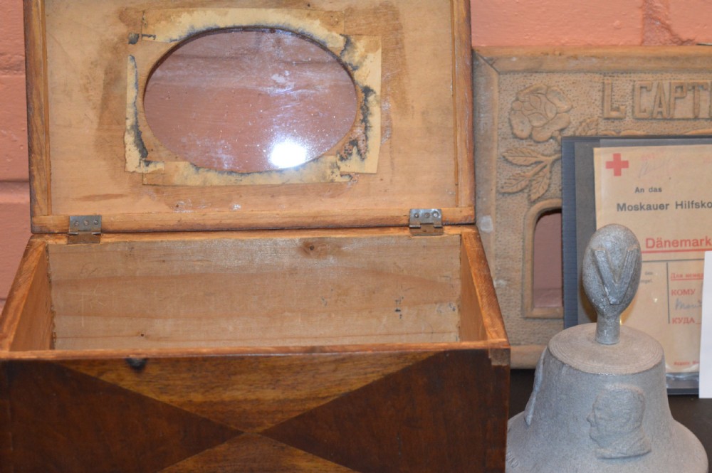 A four-piece collection of prisoner of war memorabilia including a carved wooden box, a wooden frame, a metal bell, and framed wartime documents. View VIII