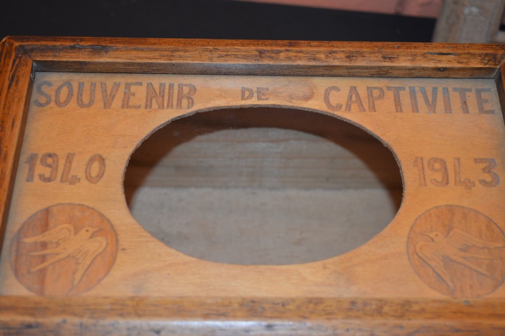 A four-piece collection of prisoner of war memorabilia including a carved wooden box, a wooden frame, a metal bell, and framed wartime documents. View XIII