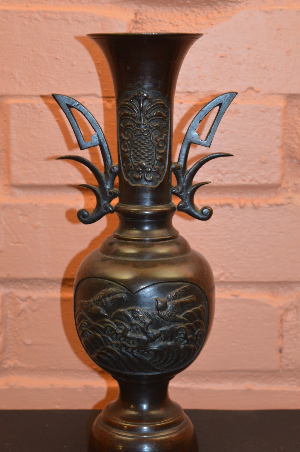 A dark brown patinated Japanese bronze vase featuring stylised handles, a flared neck, and raised relief carvings of birds over waves.