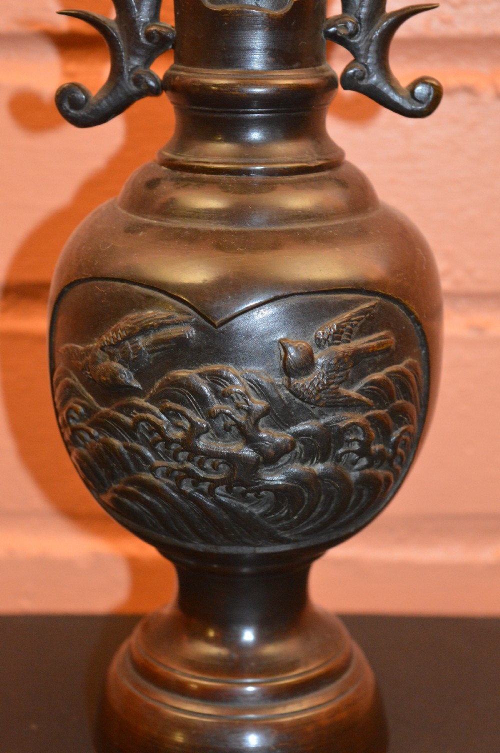 A dark brown patinated Japanese bronze vase featuring stylised handles, a flared neck, and raised relief carvings of birds over waves. View II