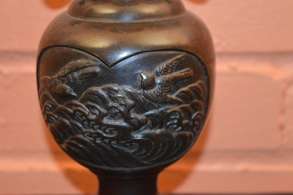 A dark brown patinated Japanese bronze vase featuring stylised handles, a flared neck, and raised relief carvings of birds over waves. View V