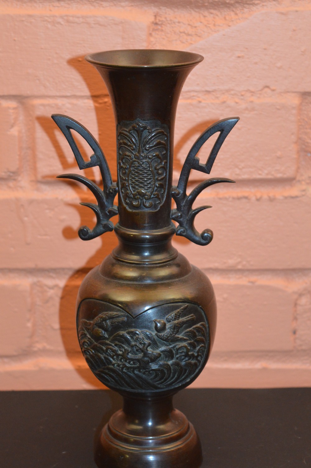 A dark brown patinated Japanese bronze vase featuring stylised handles, a flared neck, and raised relief carvings of birds over waves. View VII