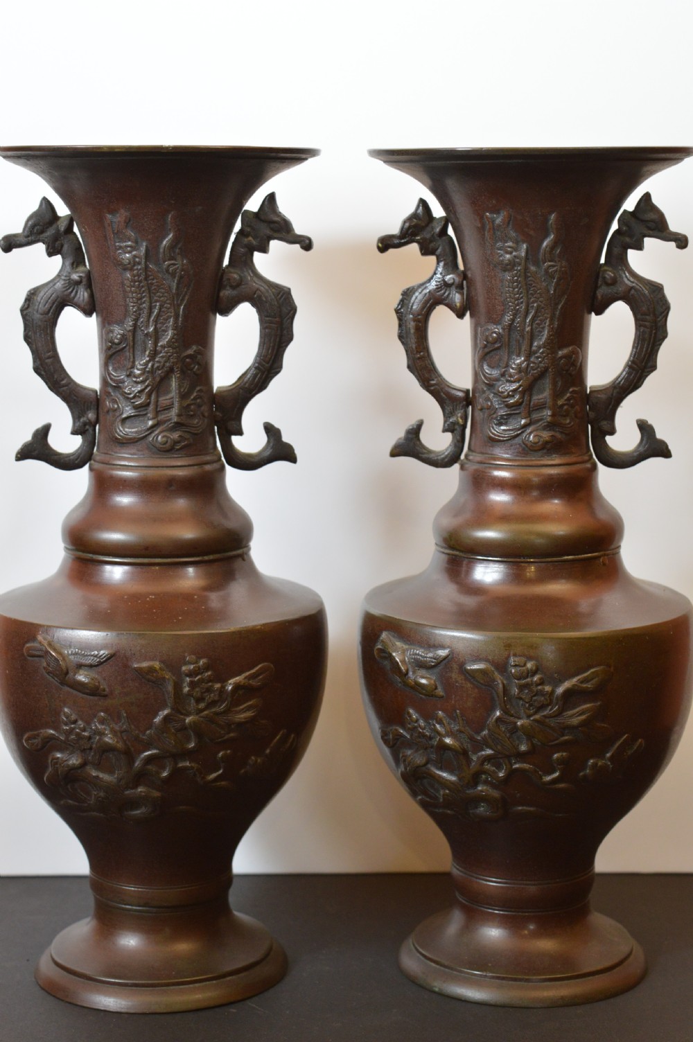 A pair of patinated dark brown Chinese bronze altar vases featuring sculpted dragon handles and low-relief carvings of birds and floral motifs.