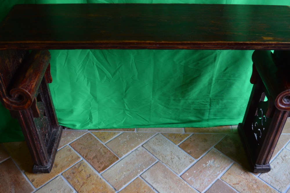 A long dark hardwood Tibetan altar table featuring a flat rectangular top supported by upright legs with prominent carved scroll terminals. View II