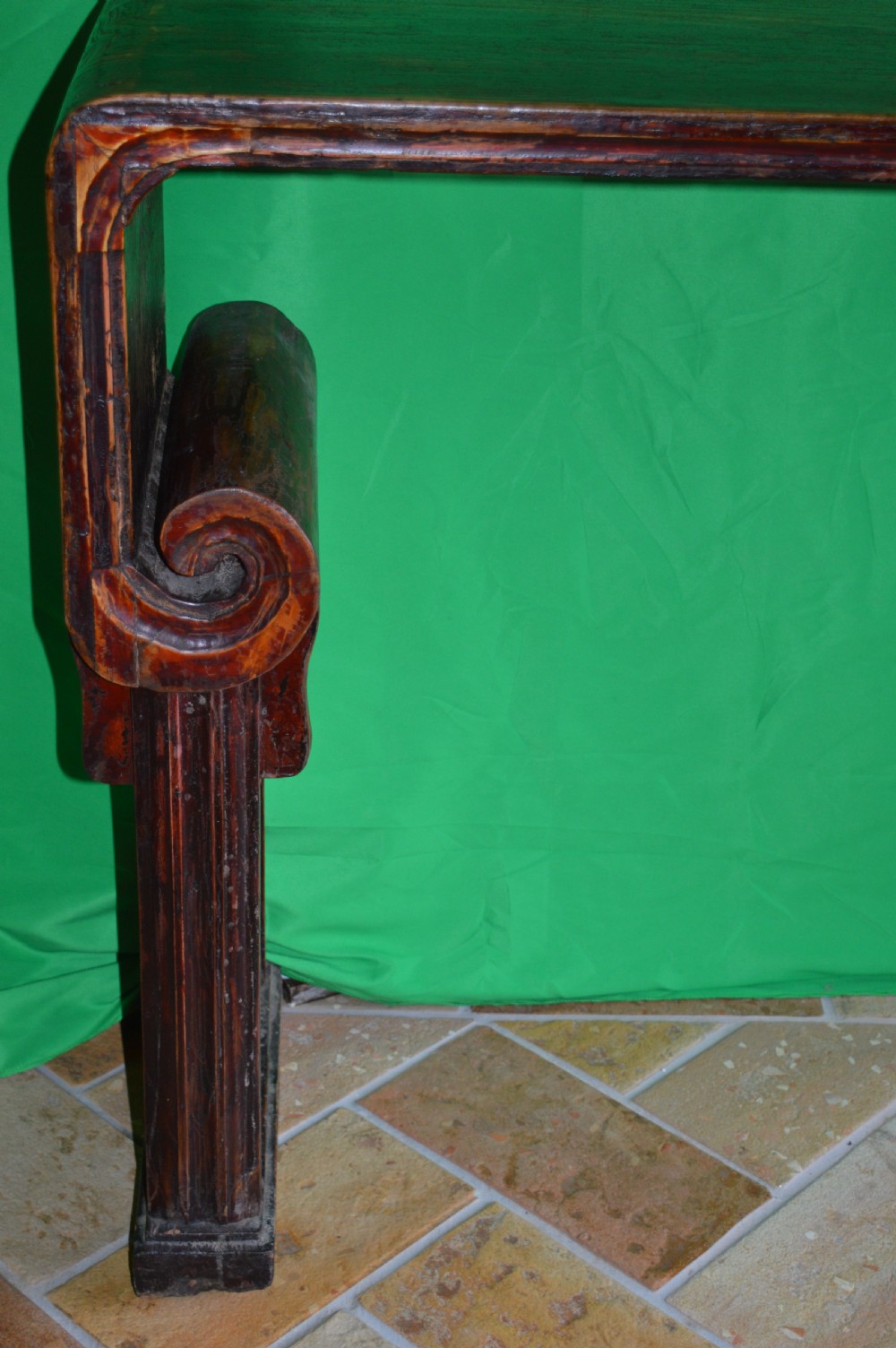 A long dark hardwood Tibetan altar table featuring a flat rectangular top supported by upright legs with prominent carved scroll terminals. View III