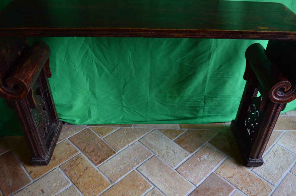 A long dark hardwood Tibetan altar table featuring a flat rectangular top supported by upright legs with prominent carved scroll terminals. View V
