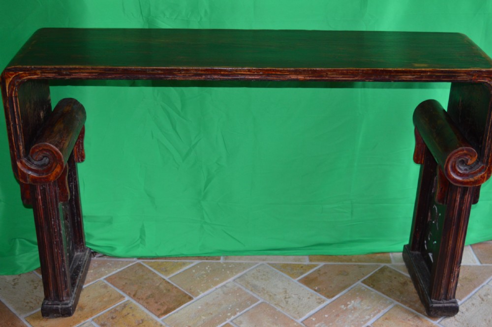 A long dark hardwood Tibetan altar table featuring a flat rectangular top supported by upright legs with prominent carved scroll terminals. View VI