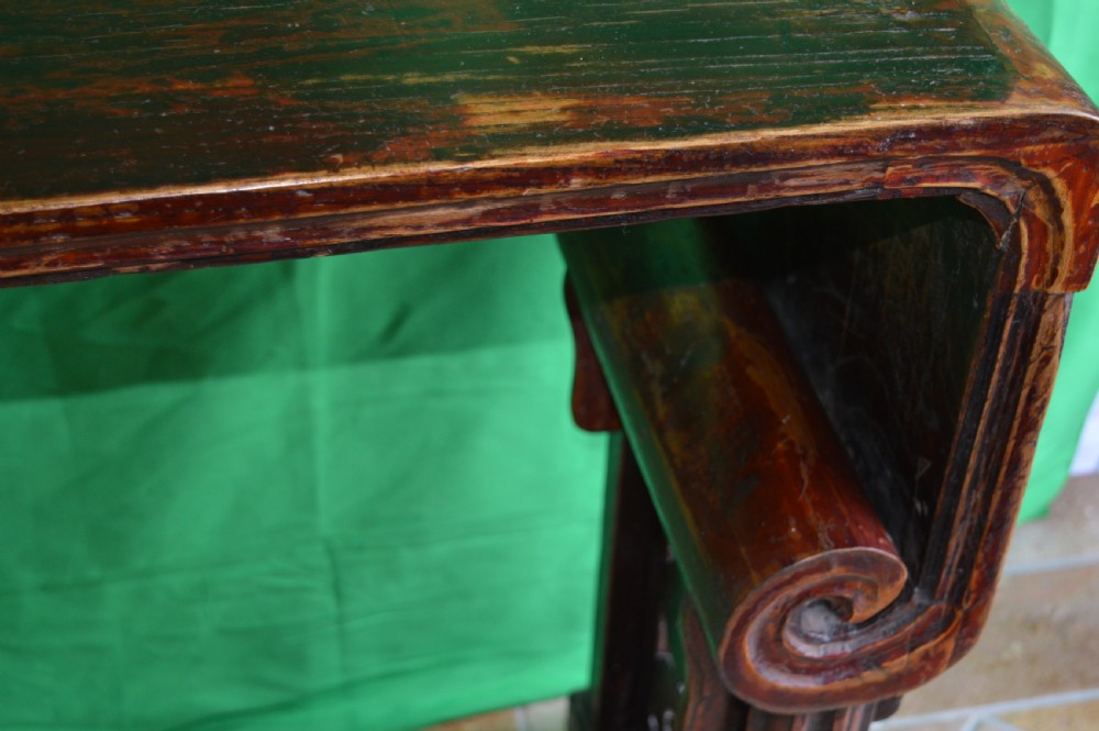 A long dark hardwood Tibetan altar table featuring a flat rectangular top supported by upright legs with prominent carved scroll terminals. View VII